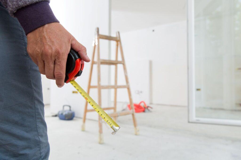 handwerker hält ein maßband und arbeitet an einer wohnungssanierung berlin